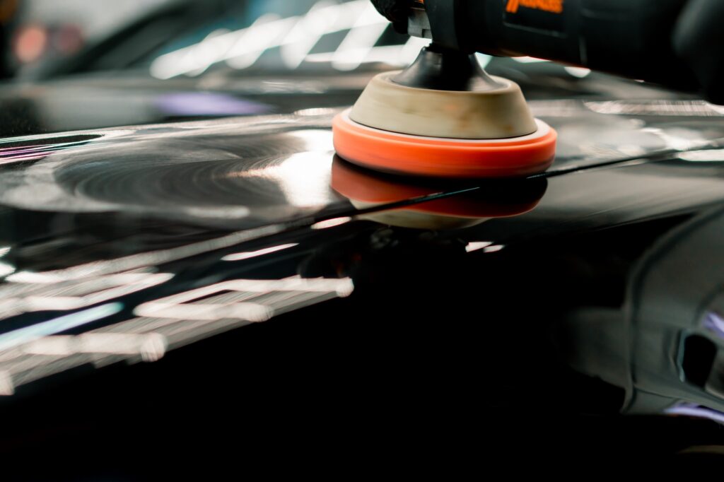 Close-up of a car wash worker using a polishing machine to polish the hood of black luxury car